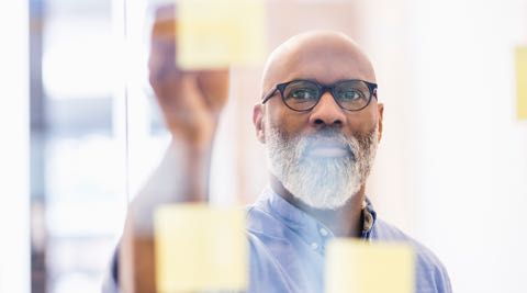 man placing sticky notes on a clear, glass wall